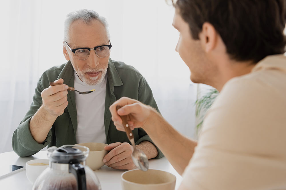 oudere en iets jongere man zitten tegenover elkaar en eten een kom soep