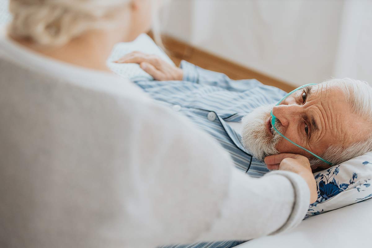 Oudere man in bed met begeleidende partner erbij